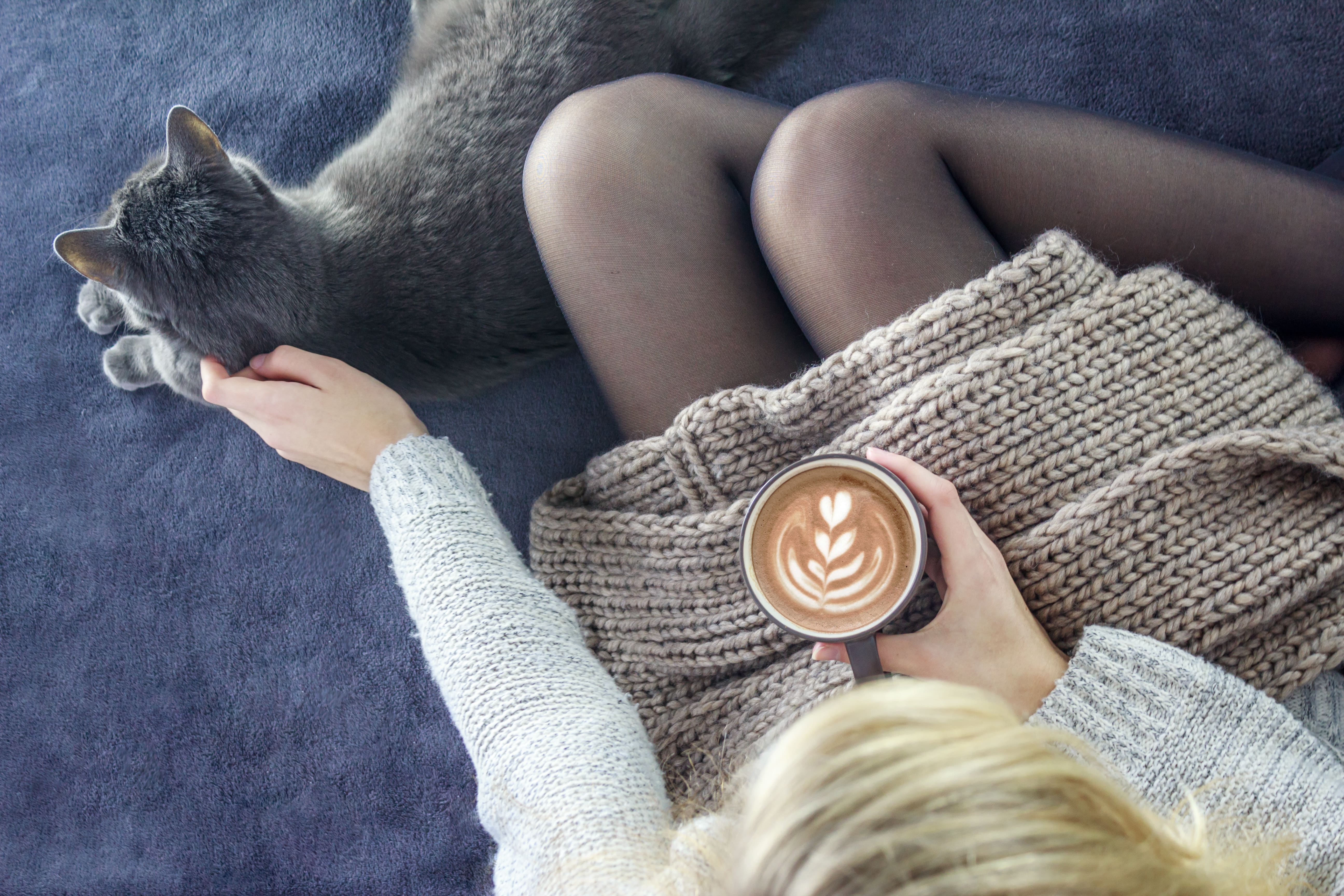 woman drinking milk with cat at her feet